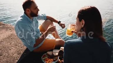 年轻的幸福夫妇坐在水边吃午饭。 海上美丽男女浪漫约会..